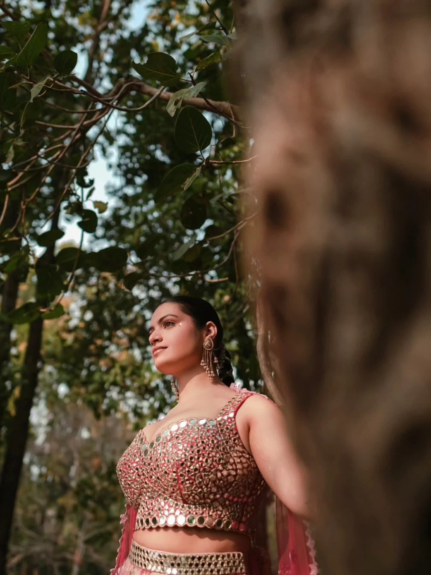 The bride in a mirror-work blouse gazing into the distance beside a tree