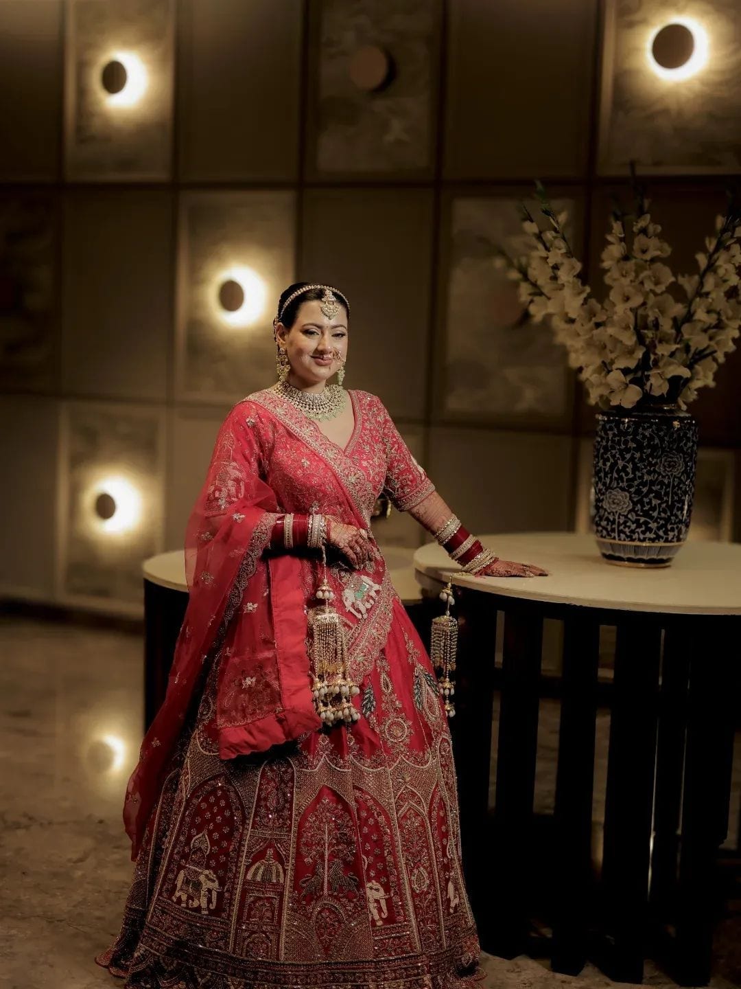 The bride smiling beside a blue ceramic vase of gladioli in a warmly lit hall