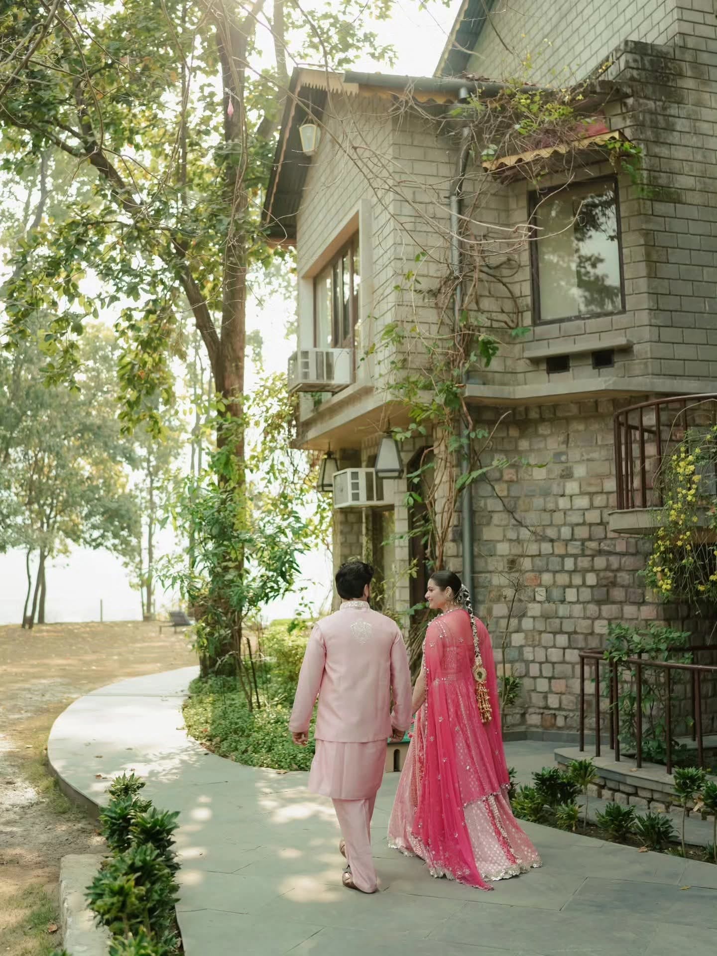 The couple walking away along a garden path, the pink dupatta trailing behind