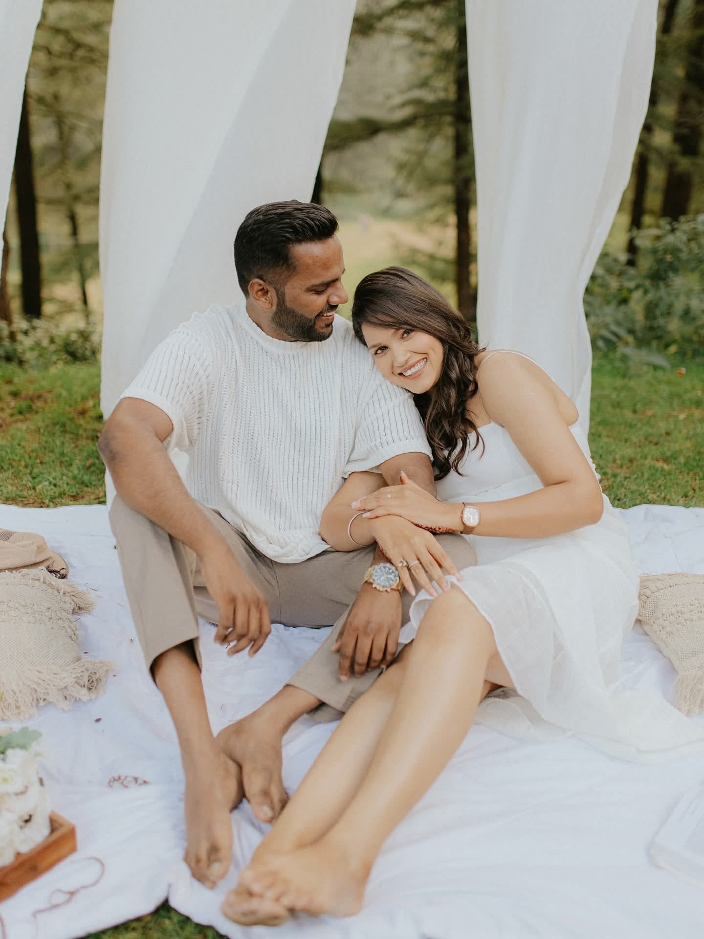 The couple on a picnic blanket in the forest, her head resting on his shoulder