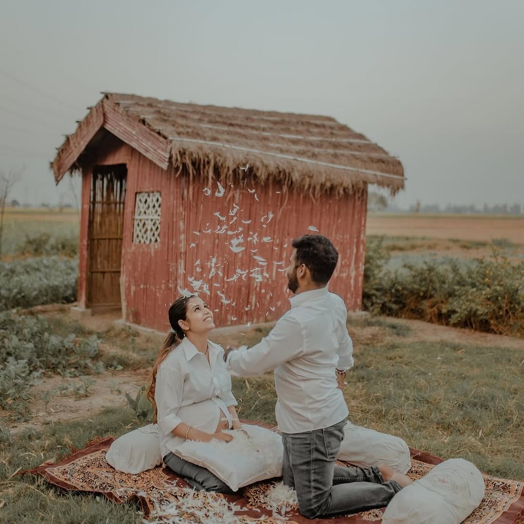An expectant couple playing with pillow feathers on a rug outside a thatched hut