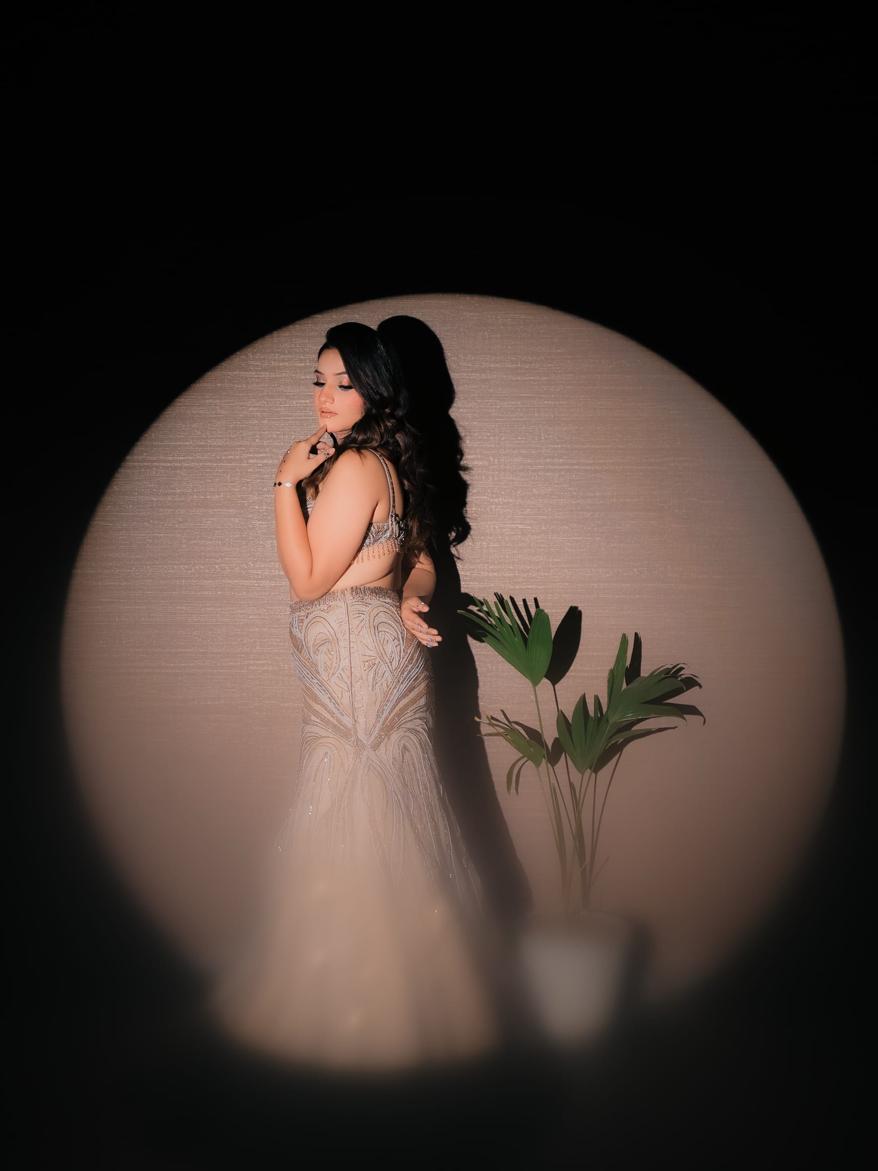 A woman in a beaded champagne lehenga inside a circular spotlight, palm beside her