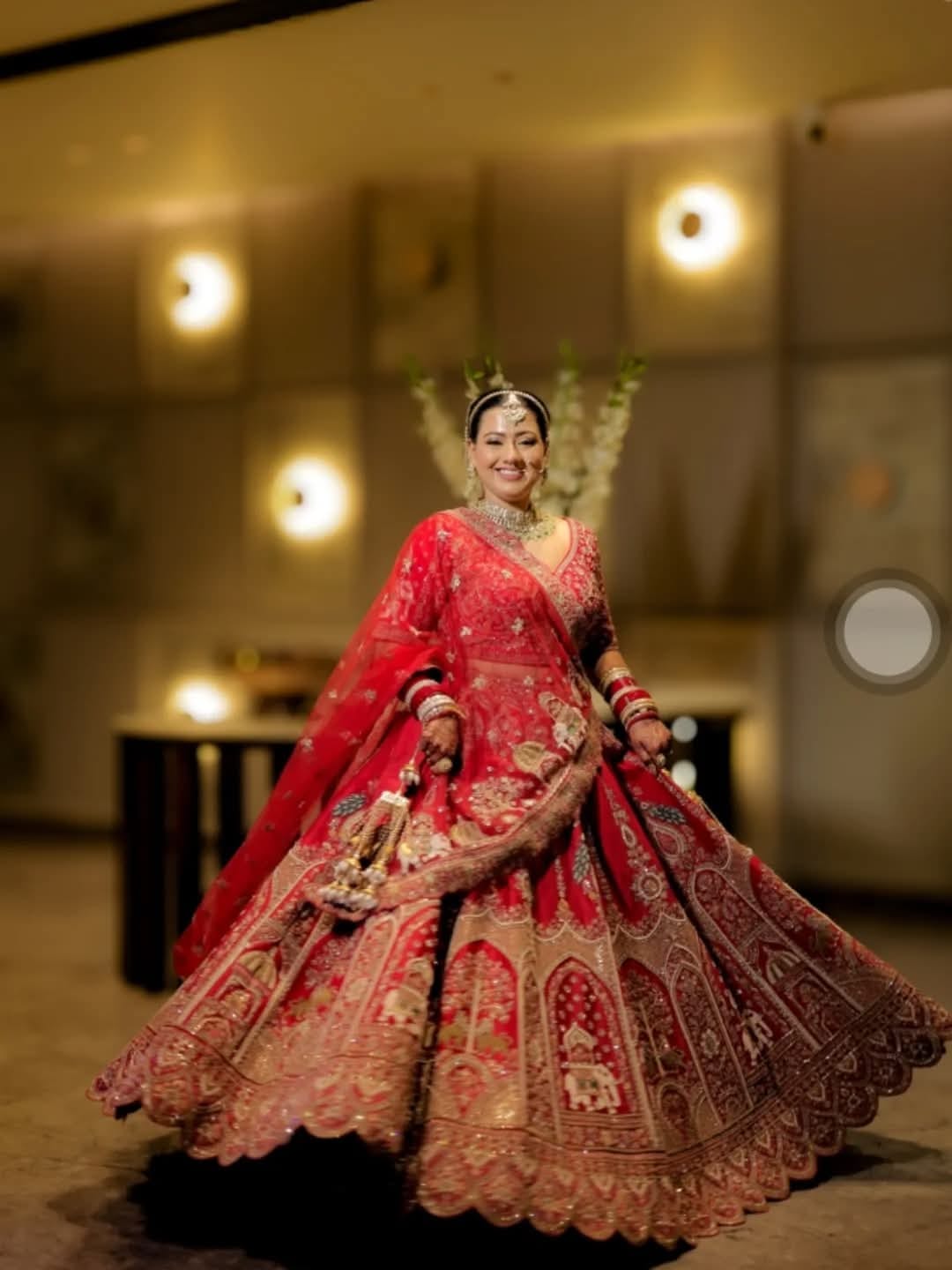 The bride in a red lehenga, full length, under warm lights