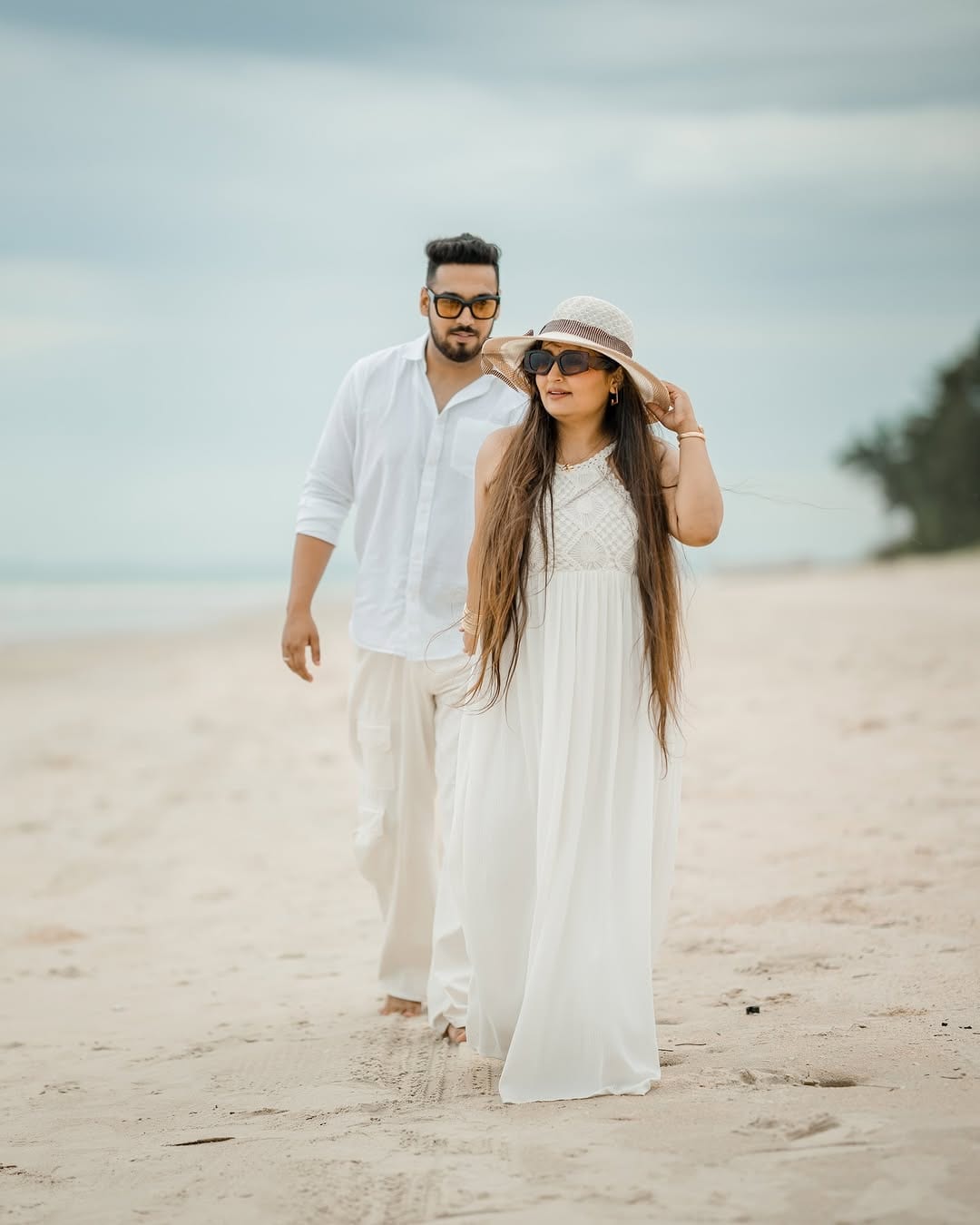 The couple walking a wide, pale beach