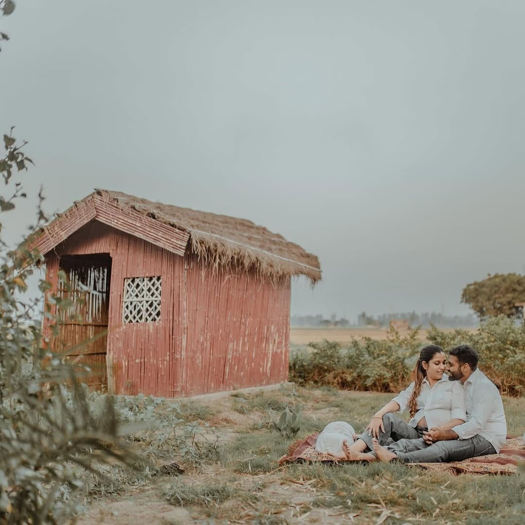 The couple small in the frame beside a thatched hut and open field